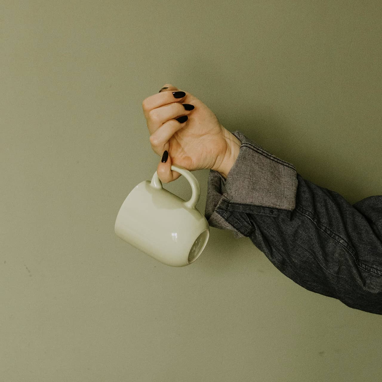Frau hält eine Tasse Kaffee in der einen Hand und eine Flasche Nagellackentferner in der anderen.